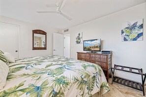 A bedroom with a bed, a wooden dresser, a television, and artwork on the walls.