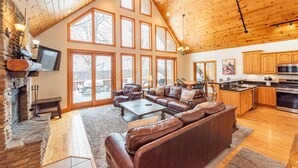 A spacious living area with a fireplace, leather sofas, and a large window overlooking a deck. - Dog Friendly Retreat w/ Indoor Pool, Hot Tub & Spa (Mchenry)