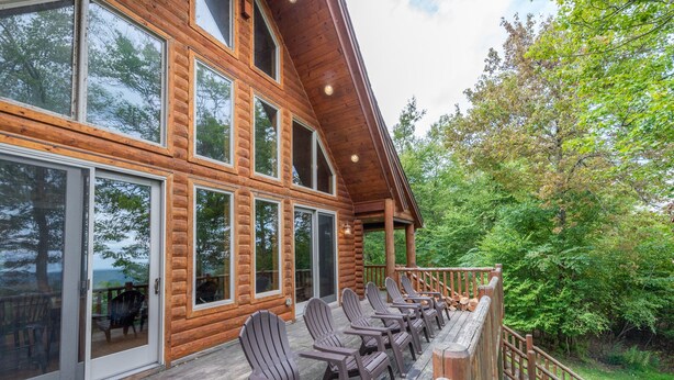 A log cabin with a deck featuring Adirondack chairs and a wooden railing. - Dog Friendly Retreat w/ Indoor Pool, Hot Tub & Spa (Mchenry)