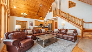 A spacious living area with a large brown leather sectional sofa, a wooden coffee table, and a staircase with wooden railings. - Dog Friendly Retreat w/ Indoor Pool, Hot Tub & Spa (Mchenry)