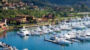A marina with numerous boats docked, surrounded by residential buildings and lush greenery. - Luxury Family Condo, access to Amenities, Beach club + Concierge Service (Herradura)