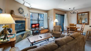 A living room with a fireplace, a television, a sofa, a coffee table, and a dining area with chairs and a table.