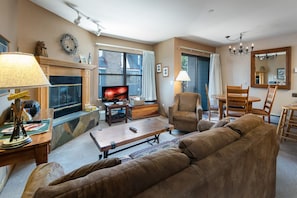 A living room with a fireplace, a television, a sofa, a coffee table, and a dining area with chairs and a table.