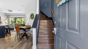 Ein modernes Interieur mit einer Holztreppe, einer Essecke mit rundem Tisch und Stühlen sowie Blick durch eine Glastür.