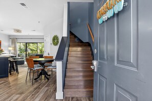 A modern interior with a wooden staircase, a dining area with a round table and chairs, and a view through a glass door.
