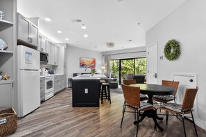A modern kitchen with white cabinets, a central island, and a dining area with wicker chairs.