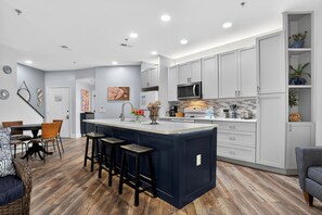 A modern kitchen with a central island, white cabinetry, and a dining area with wicker chairs.