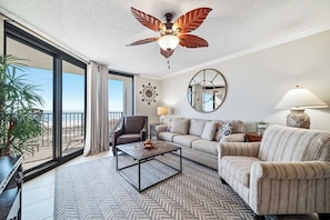 A spacious living room with a large window, a ceiling fan, a sofa, a coffee table, and a lamp.