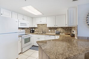 Una cocina moderna con armarios blancos, encimera de granito, microondas integrado y cafetera.