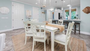 A dining area with white chairs and a table, a chandelier, and a kitchen with a window. - Best of Gulf Place at Your Doorstep Heated pools/Walk to Shops/Restaurants (Santa Rosa Beach)
