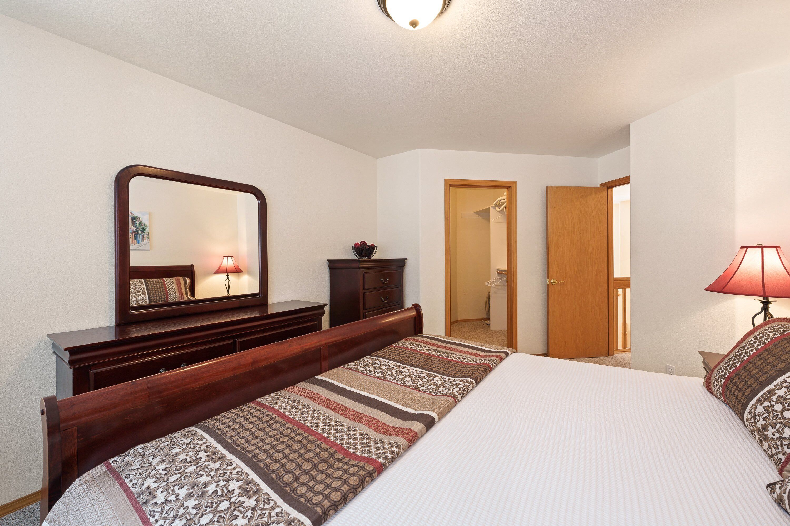 A bedroom with a bed, a dresser, a mirror, a door, and a lamp.