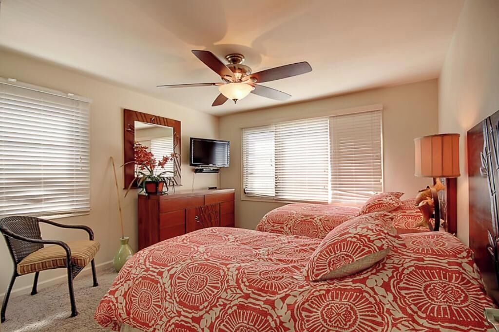 Une chambre à coucher comprenant un lit, un ventilateur de plafond, une télévision, une commode et une chaise.