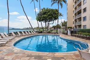 A swimming pool with lounge chairs, surrounded by palm trees and a building with balconies. - Royal Mauian 601: Stroll to Shops, Dining, & Witness Haleakalā's Majesty! (Kihei, Maui)