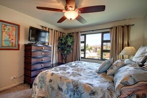 Relax in this inviting room featuring a large bed, ceiling fan, and wall-mounted TV.