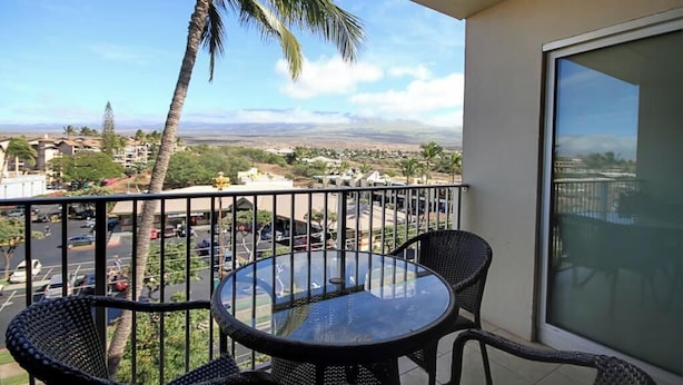Un balcon avec une table et des chaises en verre, donnant sur un parking et un paysage lointain.