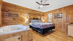 A wooden cabin room with a large bed, a wooden bathtub, and a ceiling fan.