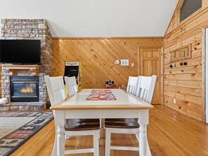 A dining area with a wooden table, white chairs, a fireplace, and a Pac-Man arcade machine.