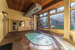 A hot tub with a brick surround, wooden ceiling, and large windows offering views of the outdoors.