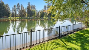 A serene park with a pond, a metal fence, and trees. - Mirror Pond - Cozy Cabin Directly on Mirror Pond - Deschutes River! (Bend)