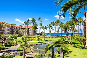 A resort with multiple buildings, a central pathway, palm trees, and a body of water. - Beachy condo with garden and ocean views (Lahaina)