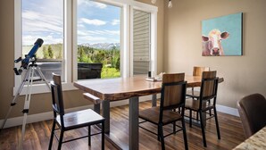 A dining area with a wooden table and chairs, a telescope on a tripod, and a painting of a cow on the wall.