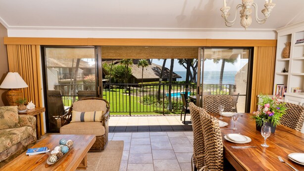 A spacious living area with a balcony overlooking a pool and ocean view, furnished with a sofa, chairs, and a dining table set for four. - Ma'alaea Surf, Unit G10, 2BR Beachfront Condo, AC, Wi-Fi, Pool, TV, Kitchen (Kihei)