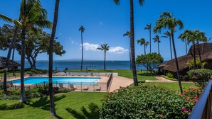 A pool area with palm trees, a view of the ocean, and a building with a sloped roof. - Ma'alaea Surf, Unit G10, 2BR Beachfront Condo, AC, Wi-Fi, Pool, TV, Kitchen (Kihei)