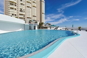 A swimming pool with a curved edge, a white poolside area, and a tall building in the background.