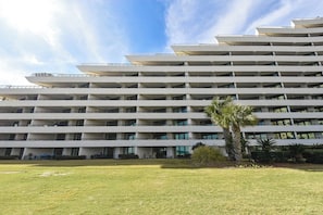 A multi-story hotel with a flat roof design, balconies on each floor, and a well-maintained lawn in the foreground.