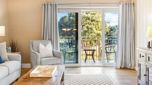 A living room with a sofa, a chair, a table, and a view of a balcony with chairs and a table. - Walk to Beach Club, Pet Friendly, Open Plan and Golf View (Hilton Head Island)