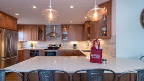 Una cocina moderna con armarios de madera, electrodomésticos de acero inoxidable, una isla grande e iluminación colgante.