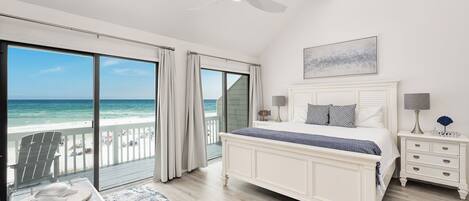 A bedroom with a large bed, a nightstand, a lamp, and a view of the ocean.