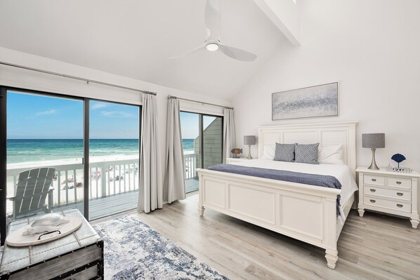 A bedroom with a large bed, a nightstand, a lamp, and a view of the ocean.