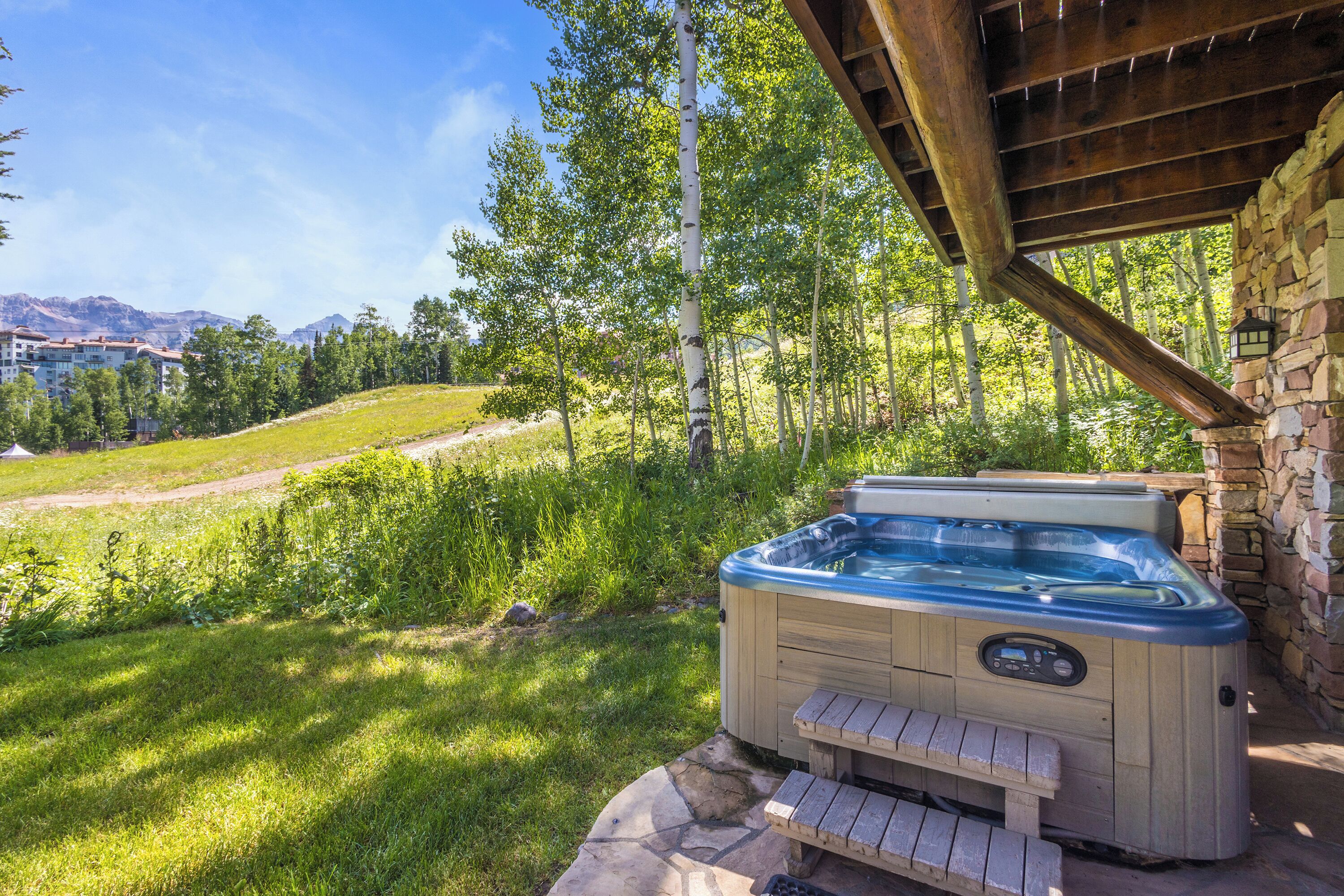 Un jacuzzi installé dans un jardin, avec un mur en pierre et une terrasse en bois.