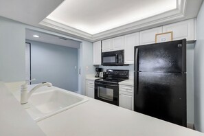 A modern kitchen with white cabinetry, a black refrigerator, a microwave, and a stove.