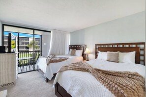 A hotel room with two beds, a balcony, and a view of the hotel buildings.