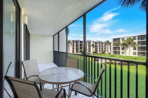 A balcony with a table and chairs, overlooking a well-maintained lawn and a building complex.
