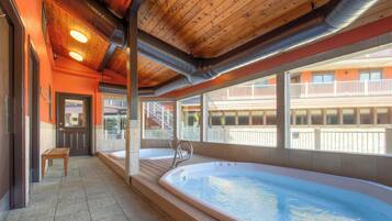 Un área de spa con un jacuzzi grande, suelo de madera y vista a un edificio con balcones.