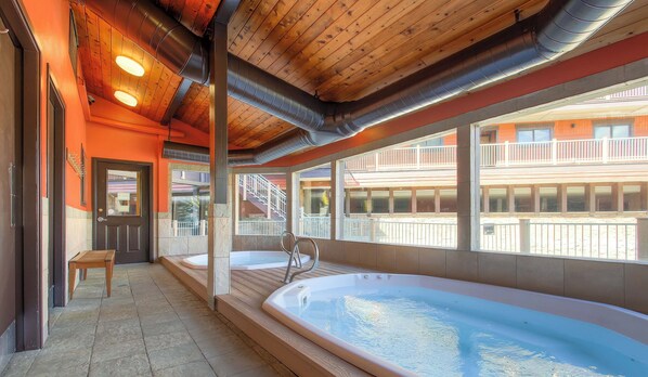Un área de spa con un jacuzzi grande, suelo de madera y vista a un edificio con balcones.