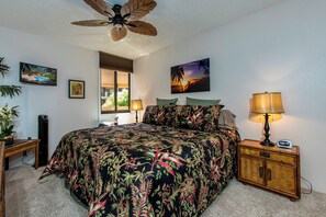A bedroom with a bed, a nightstand, a lamp, a ceiling fan, and a window.