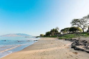 Uma praia com céu claro, mar calmo e costa rochosa.