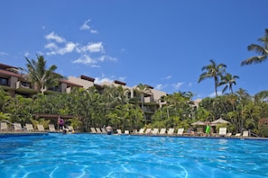 Piscina com espreguiçadeiras e palmeiras, cercada por edifícios de hotel.