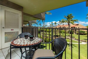 A balcony with a tiled table and chairs, overlooking a well-maintained garden and buildings.