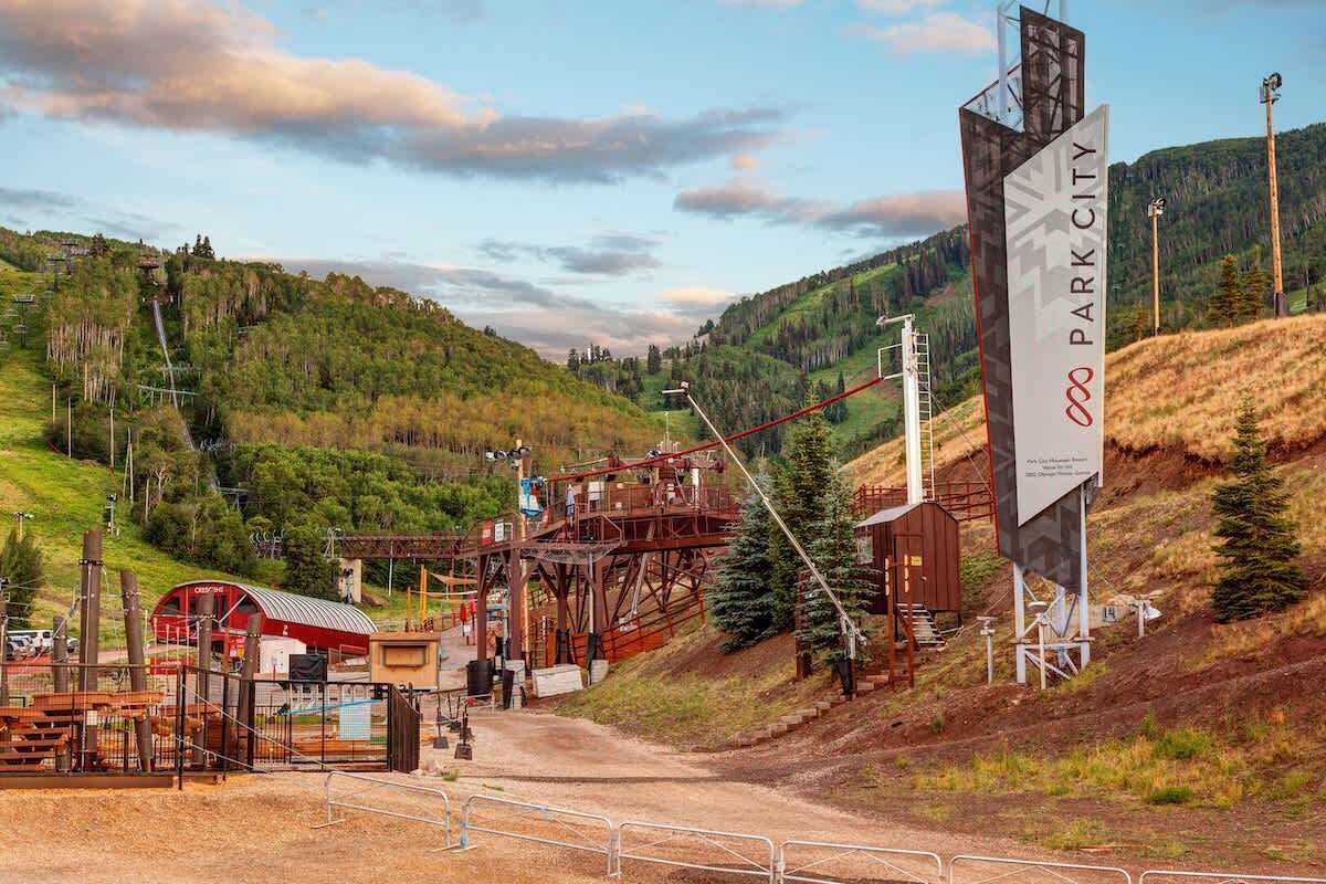 Ett bergigt landskap med en röd byggnad, en stor skylt med texten ”PARK CITY” och en grusväg som leder uppför.