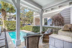 Relax by the pool in a serene outdoor space with wicker furniture and a grill station.