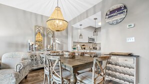 A dining area with a wooden table and chairs, a chandelier, and a decorative wall clock. - Rates Reduced! 2BR Condo with Great Gulf Views! Walk to Beach, Beautiful Pool (Miramar Beach)