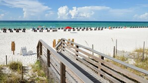 A beach with a wooden boardwalk leading to the shore, lined with beach chairs and umbrellas. - Rates Reduced! 2BR Condo with Great Gulf Views! Walk to Beach, Beautiful Pool (Miramar Beach)