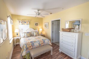 A bedroom with a bed, bedside tables, a dresser, a bench, a ceiling fan, and a door.