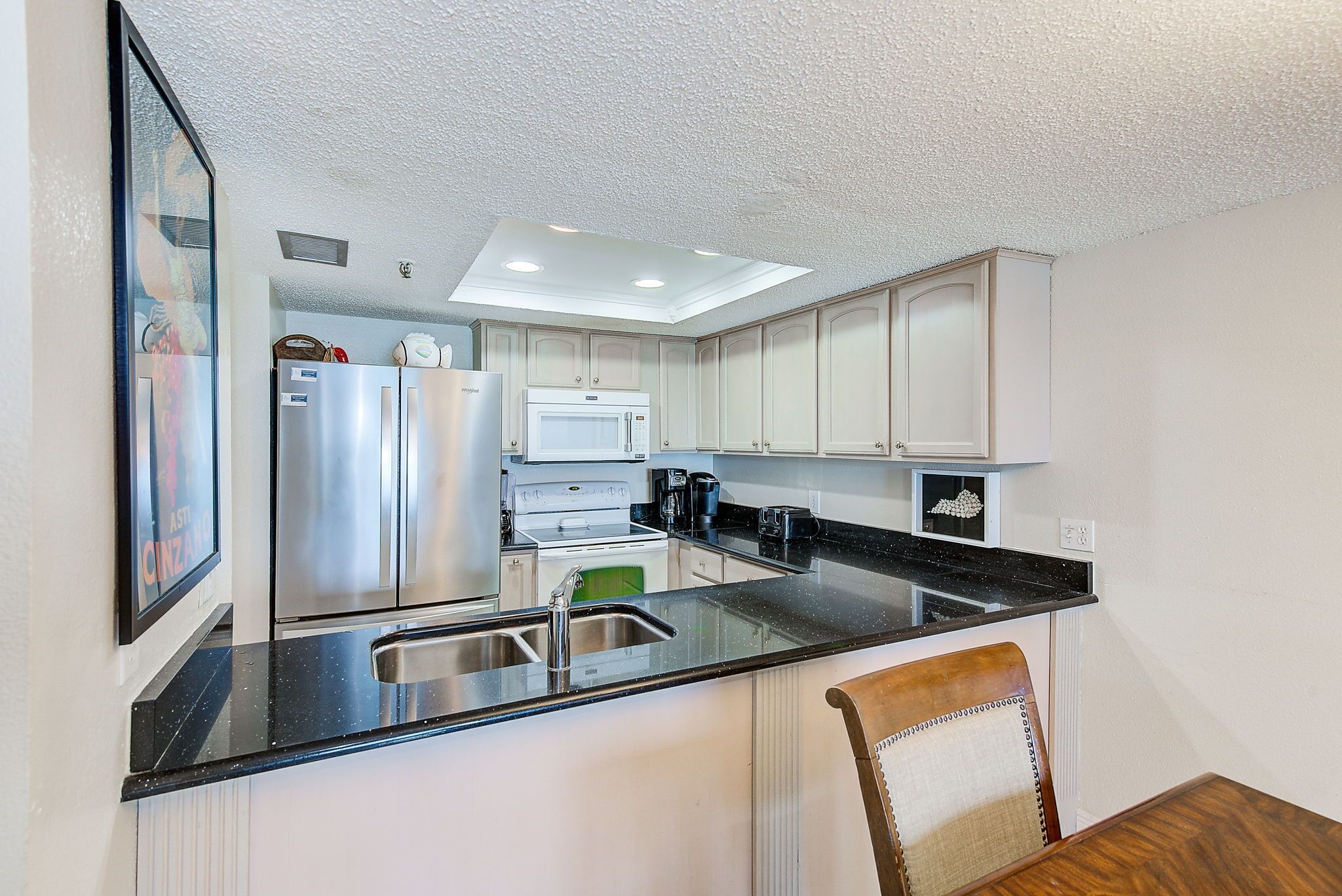 A modern kitchen with stainless steel appliances, a black countertop, and white cabinetry.