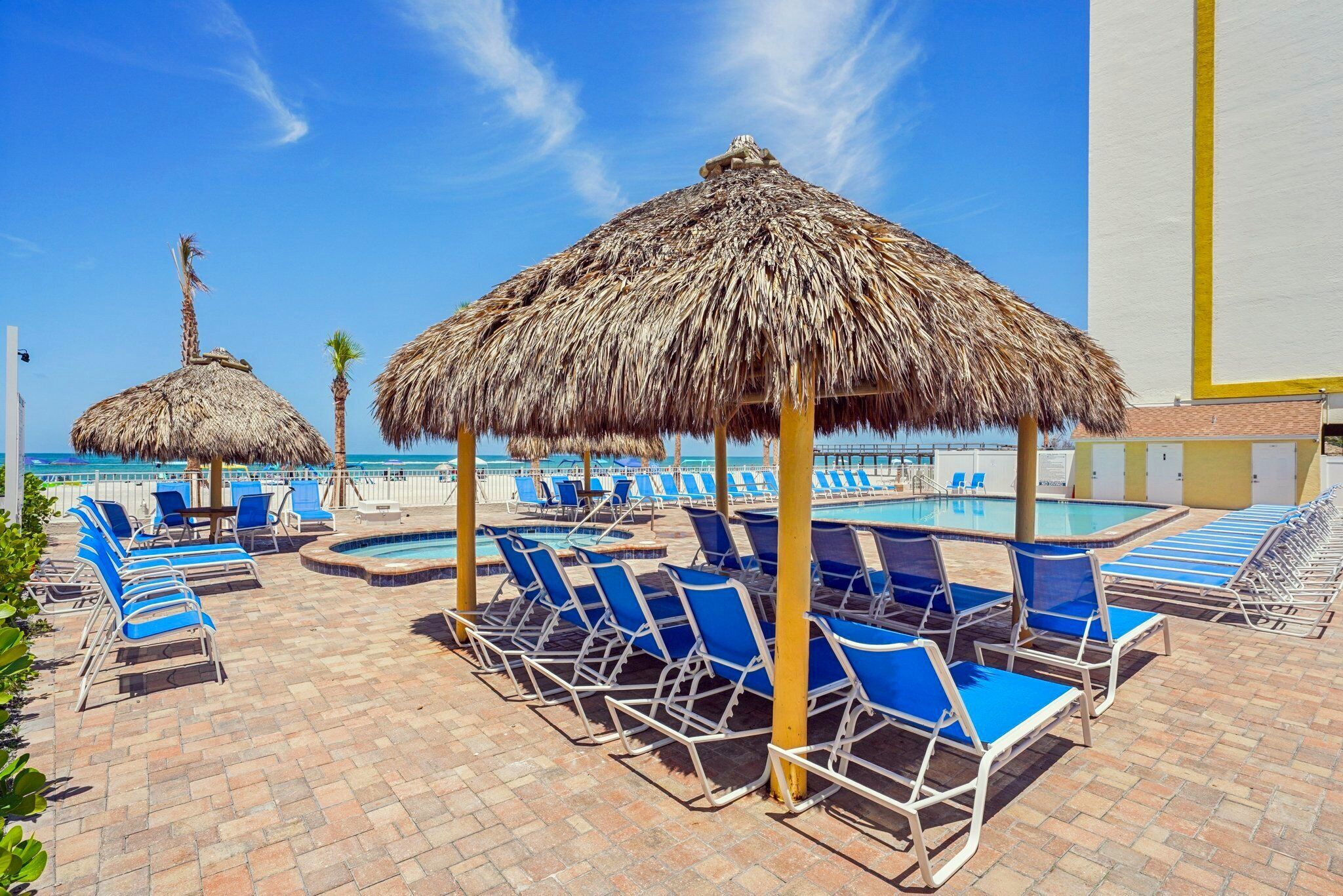 A poolside area with thatched umbrellas, blue lounge chairs, and a clear view of the pool.